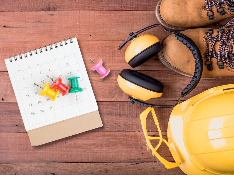 Safety gear including a hard hat, earmuffs, boots, and a calendar for renewing the working at heights certificate.