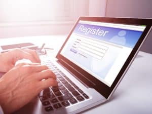 Person registering online for a working at heights certificate renewal course, typing on a laptop in a bright room.