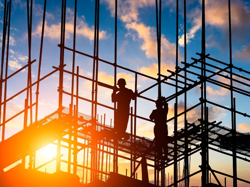 Silhouettes of construction workers on scaffolding at sunset, highlighting the importance of a working at heights certificate.