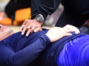 Basic life support training showing hands performing chest compressions on a person in an outdoor emergency situation.