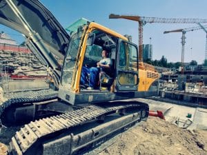 Operate excavator digging soil in a field, creating a large pit with green fields in the background.