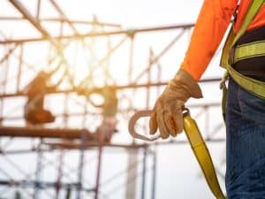 Worker holding a safety harness clip on a construction site, emphasising the importance of a white card certificate.