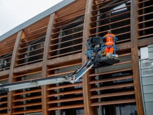 Worker operating an elevated platform to perform maintenance on a building's wooden exterior facade.