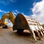 Excavator digging on a construction site, focusing on the large bucket resting on the ground.