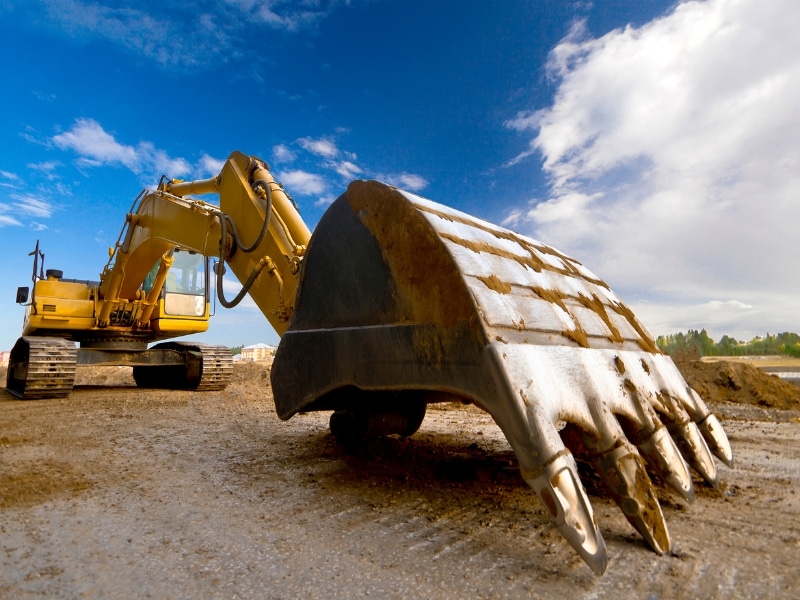 Excavator digging on a construction site, focusing on the large bucket resting on the ground.