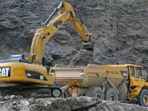 Excavator digging and loading dirt into a Volvo dump truck at a construction site.