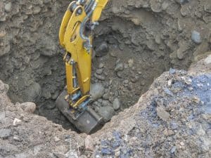 Excavator digging deep into the ground, revealing rocks and soil during excavation.