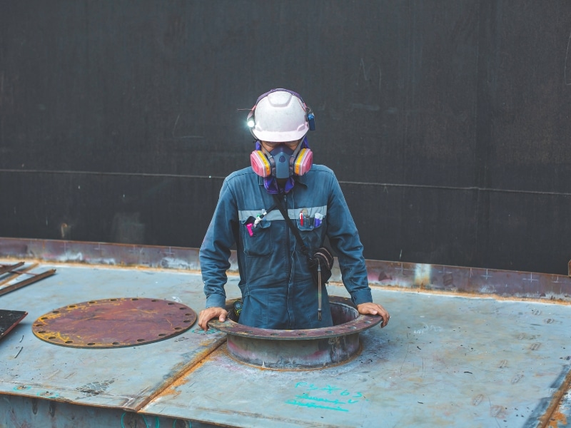 Worker with respirator mask and safety equipment emerges from confined spaces, focusing on industrial safety.