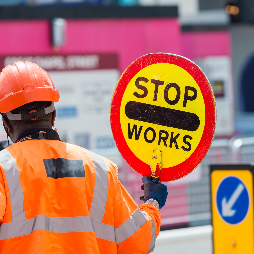 Traffic Management Implementer Skill Set worker holding "Stop Works" sign at a construction site for traffic control