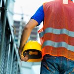 Worker holding a hard hat while wearing a safety vest, representing personal protection in a site safety management plan.