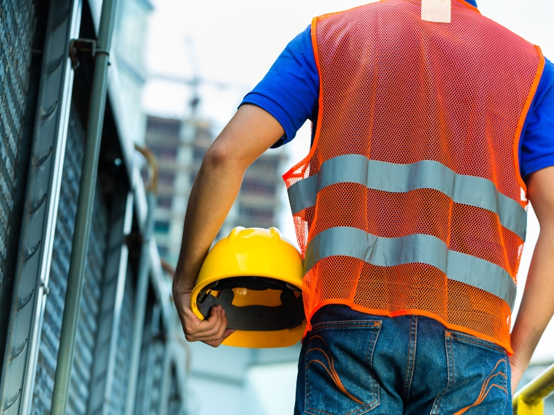 Worker holding a hard hat while wearing a safety vest, representing personal protection in a site safety management plan.