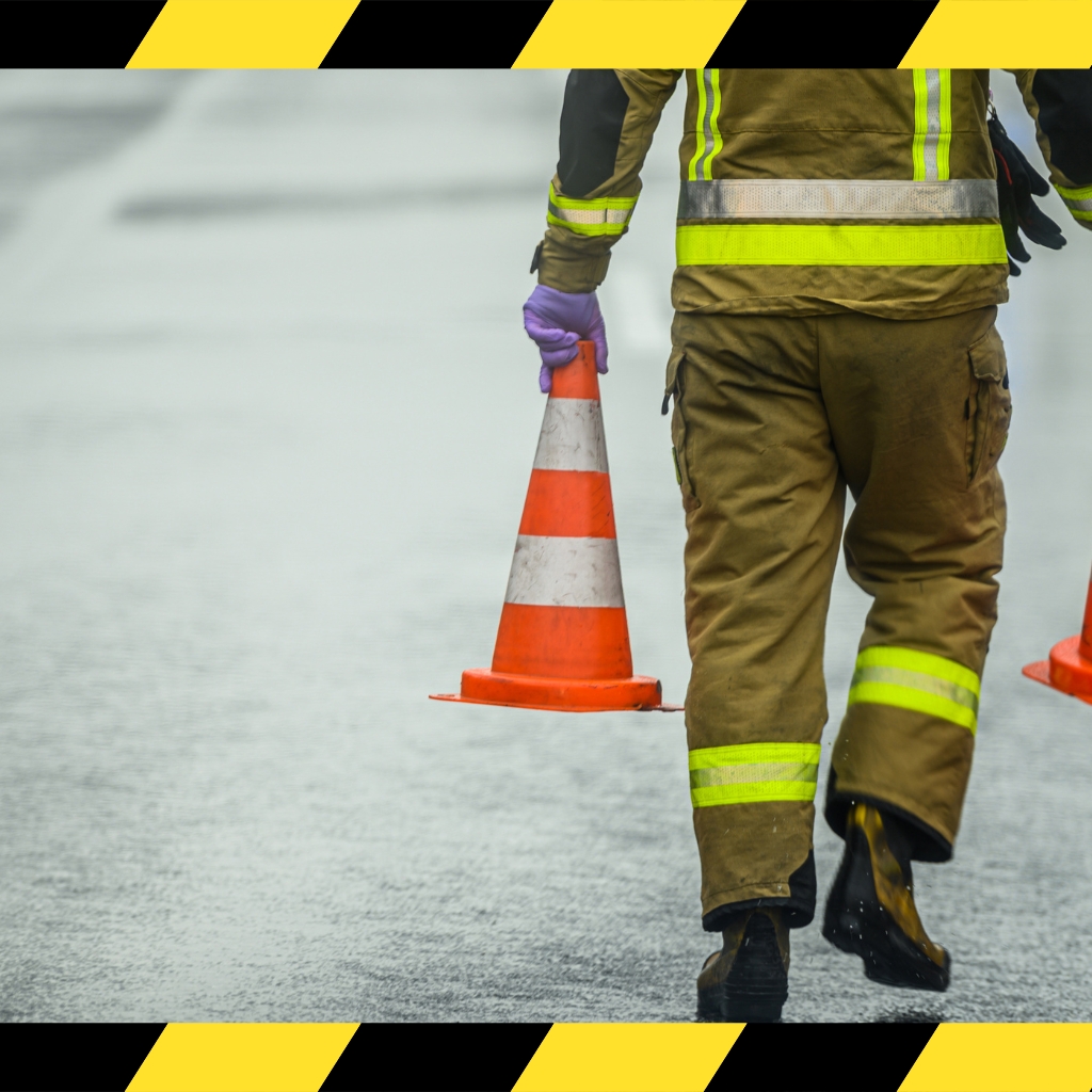 Traffic Management Implementer Skill Set worker carrying traffic cones on a wet road for safety and control setup