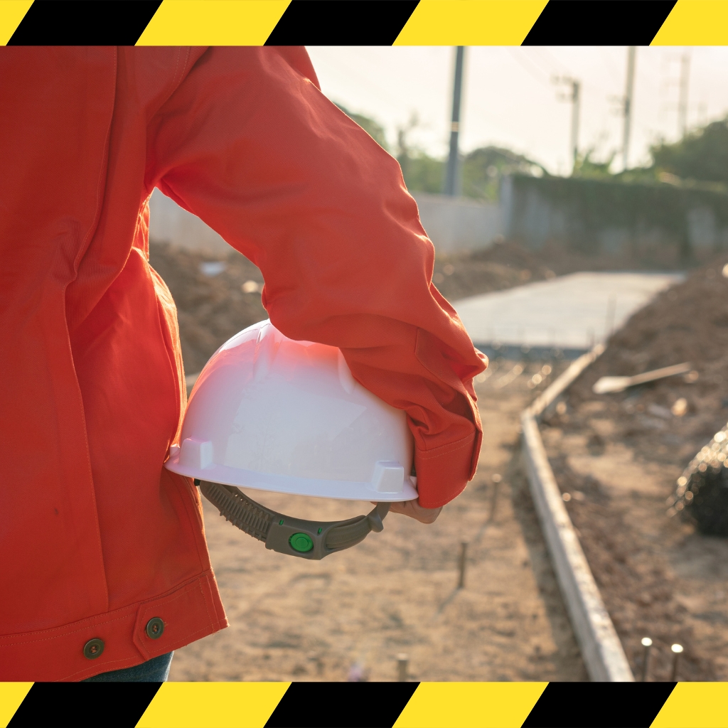 A person in an orange jacket holds a hard hat, showcasing their White Card License for construction safety compliance.