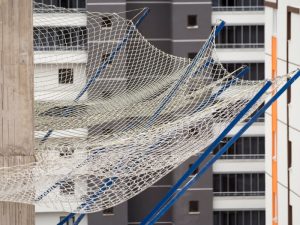 A large white safety net draped over a scaffolding structure, acting as a fall prevention system during construction.