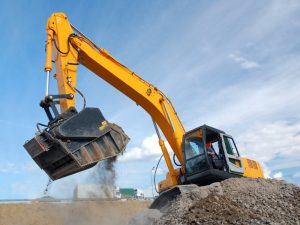 Bright yellow excavator sinking into loose soil, spilling dirt from its bucket during excavation on a construction site.