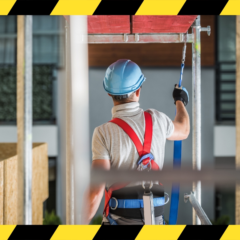 A man in a hard hat and safety harness stands on a ladder, demonstrating safe work practices during training.