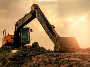 Excavator sinking into soft ground at sunset, struggling to operate efficiently on unstable terrain