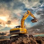 Excavator sinking slightly in muddy terrain under dramatic skies, illustrating challenges of operating on unstable surfaces.