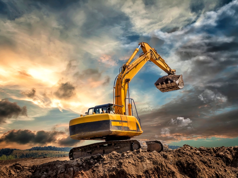 Excavator sinking slightly in muddy terrain under dramatic skies, illustrating challenges of operating on unstable surfaces.