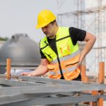 Worker in a high-visibility vest inspecting metal structures, emphasising the importance of ergonomics in reducing manual handling injuries.