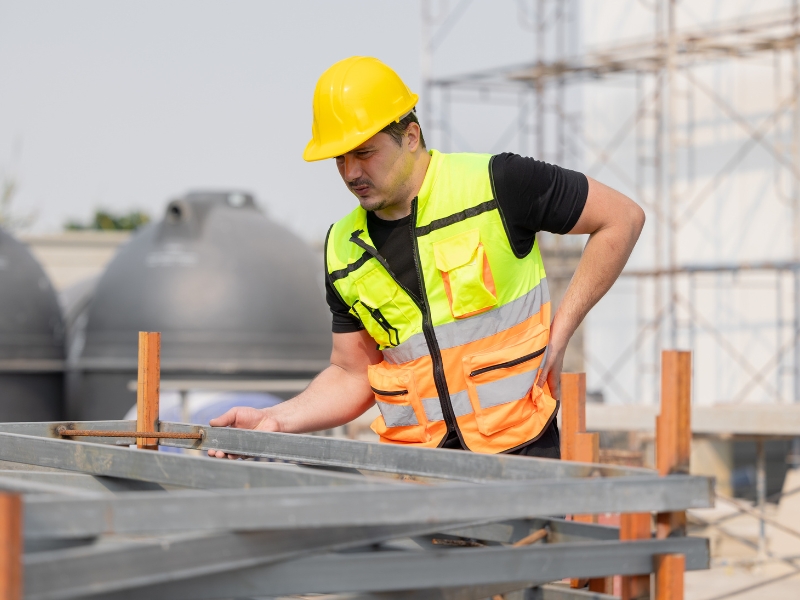 Worker in a high-visibility vest inspecting metal structures, emphasising the importance of ergonomics in reducing manual handling injuries.