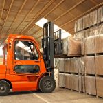 Large orange forklift lifting wrapped pallets in a warehouse, emphasising forklift weight limits for heavy-duty industrial operations.