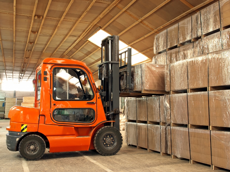 Large orange forklift lifting wrapped pallets in a warehouse, emphasising forklift weight limits for heavy-duty industrial operations.