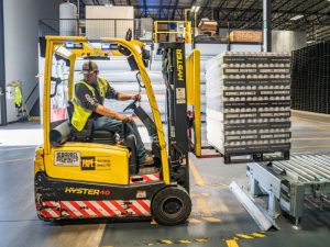 Warehouse worker operating a forklift while lifting stacked goods, demonstrating forklift weight limits and safe material handling.